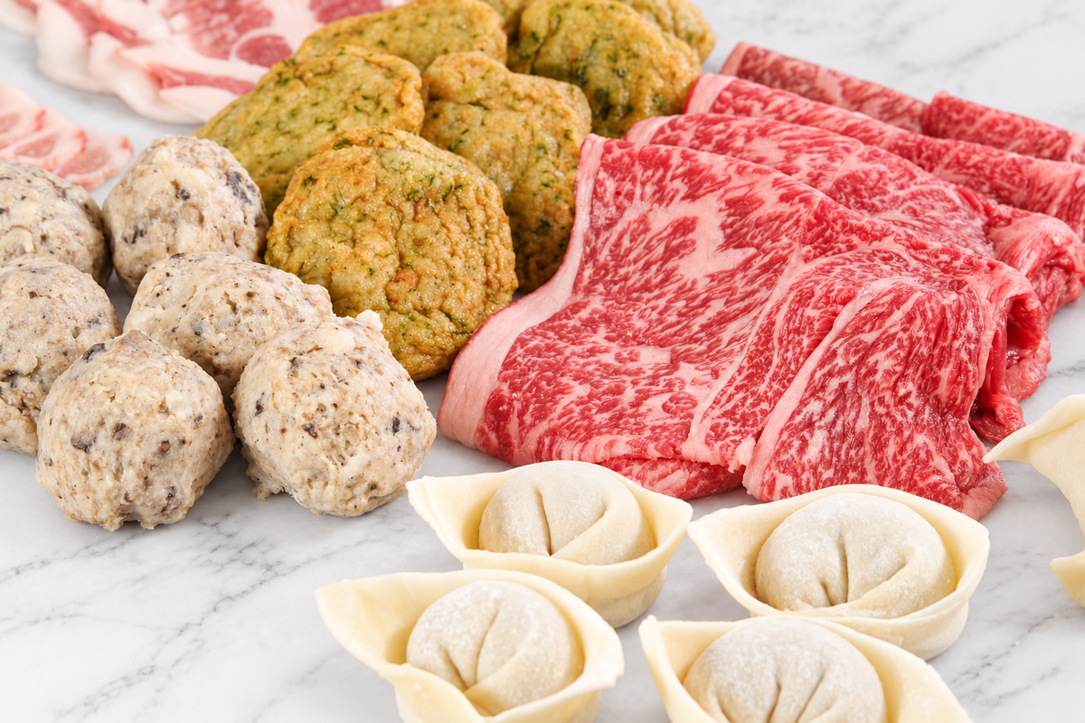 Close-up of Wagyu slices, shiitake meatballs, fish cakes and Shanghai wontons on white marble